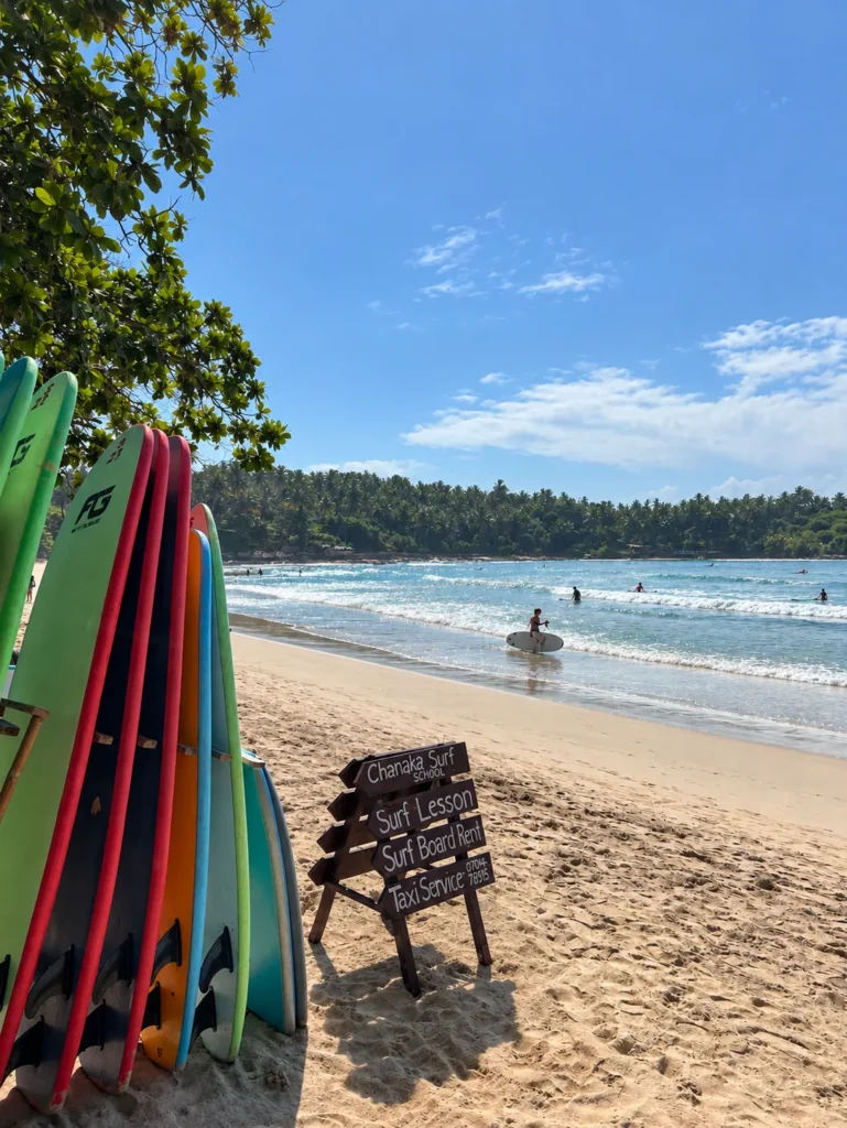 Colourful surfboards for rent in Hiriketiya with kids, Sri Lanka, with surfers enjoying the waves.